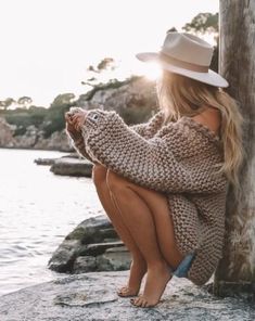 a woman sitting on the ground next to a tree wearing a white hat and sweater