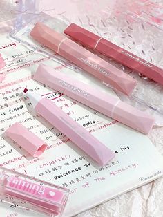 three pink lip glosses sitting on top of a piece of paper next to each other