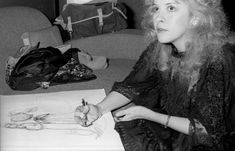 a black and white photo of a woman sitting at a table with a pencil in her hand