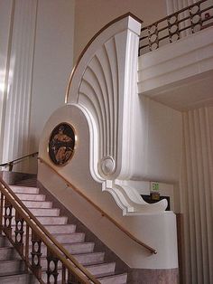 a clock on the side of a white wall next to a stair case in a building