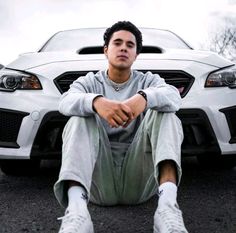 a young man sitting in front of a white car