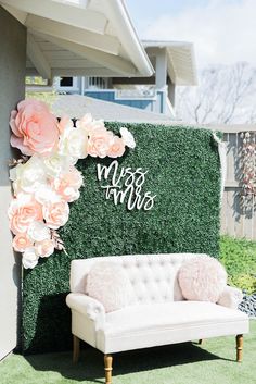 a white couch sitting in front of a lush green wall with flowers on it's side