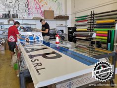 two men working on a large table in a room with lots of different colored papers