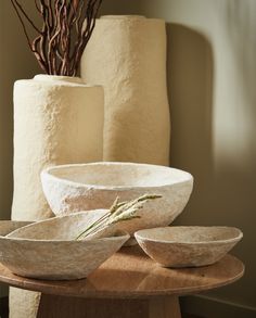 three white bowls sitting on top of a wooden table next to two tall vases