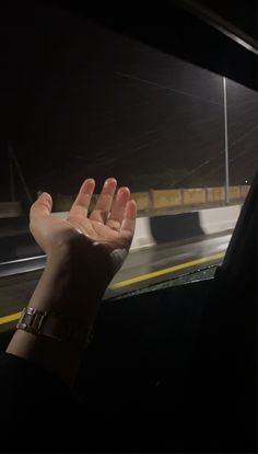 a person is holding their hand out the window at night on a street with lights in the background