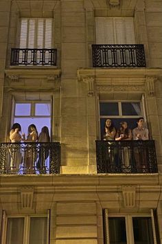 people are standing on the balcony of an apartment building at night, looking out from their balconies