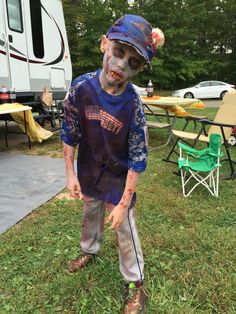 a young boy dressed up as a zombie in the grass with his face painted like a baseball bat