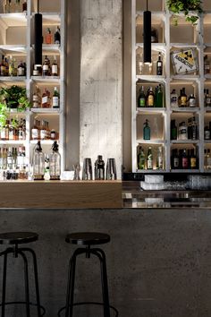 two bar stools in front of a counter with liquor bottles and plants on it