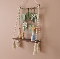 a wooden shelf with hanging plants and vases on it, against a pink wall