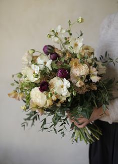 a woman holding a bouquet of white and purple flowers with greenery in her hands