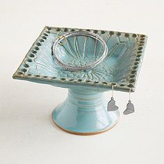 a small blue bowl with two silver rings on the bottom and a pair of earrings hanging from it