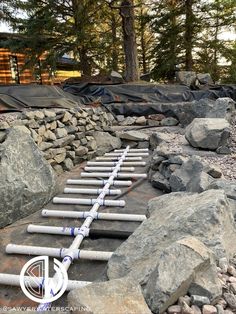 there are many pipes laying on the ground next to some rocks and trees in the background