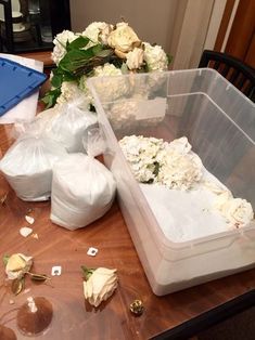 plastic containers filled with white flowers on top of a wooden table in front of a blue box