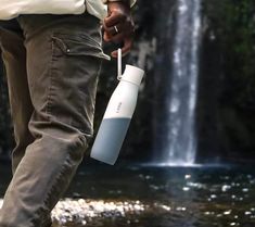 a man holding a water bottle in front of a waterfall