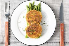 two pieces of fried fish on a plate with asparagus and carrots next to silverware