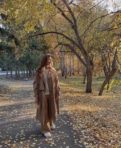 a woman standing in the middle of a leaf covered park