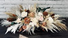 an arrangement of dried flowers and feathers on a wooden table in front of a brick wall