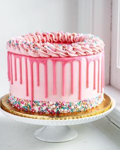 a cake with pink icing and sprinkles on a gold platter