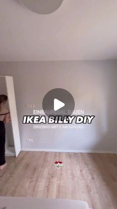 a woman standing in an empty room with white walls and wood floors, looking at the floor