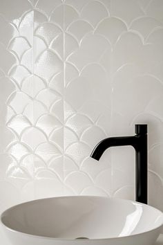 a black faucet sitting on top of a white sink in front of a wall