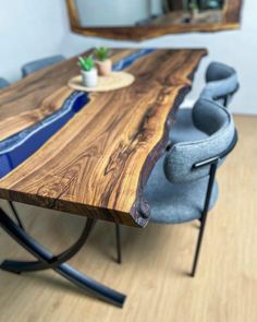 a wooden table with blue chairs and a potted plant on the end, in front of a mirror