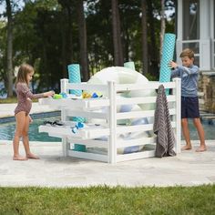 two children are playing by the pool with an umbrella and towel rack in front of them