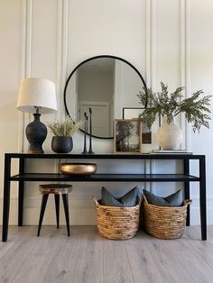 a black console table with two baskets on it and a round mirror over the top