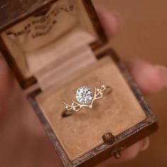 a close up of a person holding an open box with a diamond ring in it