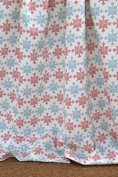 a red, white and blue patterned curtain hanging on a wooden floor with a cat sitting in front of it