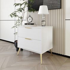 a white chest of drawers sitting next to a lamp on top of a wooden floor