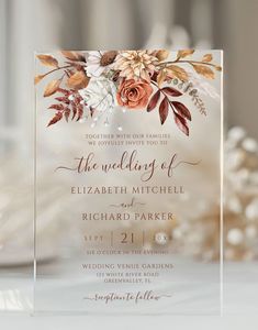 an elegant wedding card with flowers and leaves on it, is displayed in front of a table