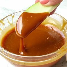 someone is dipping some kind of sauce in a glass bowl with an apple slice on top