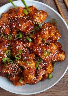 a white plate topped with chicken covered in sesame seeds and green onions next to chopsticks