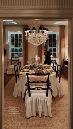 a dining room with a chandelier hanging from the ceiling and table covered in white cloths