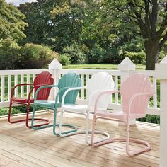 four different colored plastic chairs on a wooden deck with white railing and trees in the background