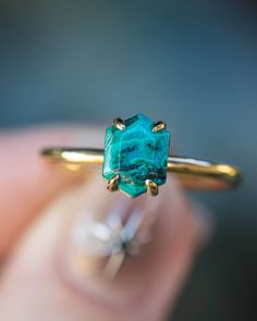 a woman's hand holding a gold ring with an emerald colored stone