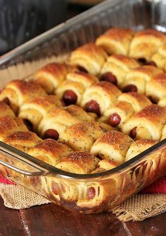 a casserole dish filled with hot dogs and buns on a wooden table