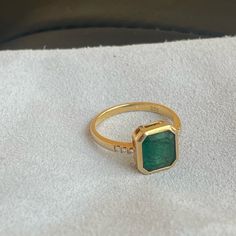 a gold ring with a green stone in the center on a white cloth covered surface