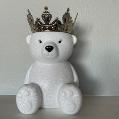 a white teddy bear with a crown on its head sitting in front of a wall