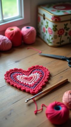 a crocheted heart sitting on top of a wooden table next to yarn