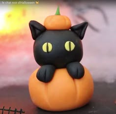 a black cat figurine sitting on top of an orange pumpkin with yellow eyes