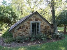 an old stone building sitting in the middle of a field with trees and grass around it