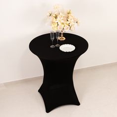 a black table with white flowers and two champagne glasses on it, in front of a white wall