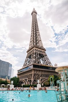 the eiffel tower towering over a pool with people swimming in it and some buildings around