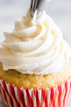 a cupcake with white frosting and a piping tool sticking out of it