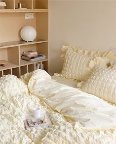 an unmade bed with white sheets and pillows on top of it next to a book shelf