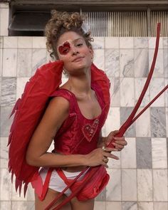 a woman dressed in red and white with wings on her head, holding two scissors