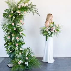 a woman standing in front of a floral arch with flowers and greenery on it