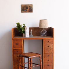 a wooden desk with a chair and vase on it next to a wall mounted painting