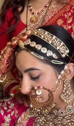 a woman in a red and gold outfit with jewelry on her head, looking down at the ground